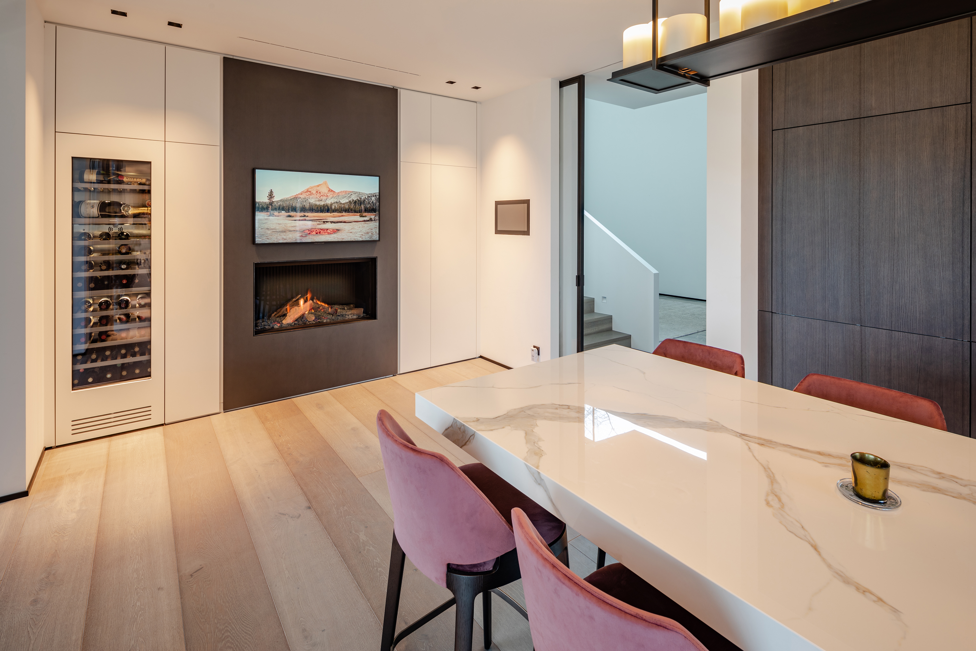 Moderner Essbereich mit Marmor-Tisch, Kamin, Weinkühlschrank und rosa Polsterstühlen in heller, stilvoller Raumgestaltung.
